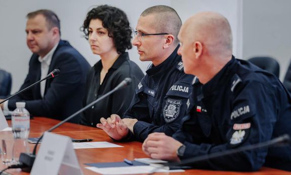 polscy policjanci siedzą przy stole. obok dwoje cywili
