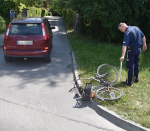 samochód osobowy obok leży rower a przy nim stoi policjant